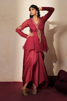 Woman in a mauve pink traditional outfit standing againsta beige wall on a red carpet.