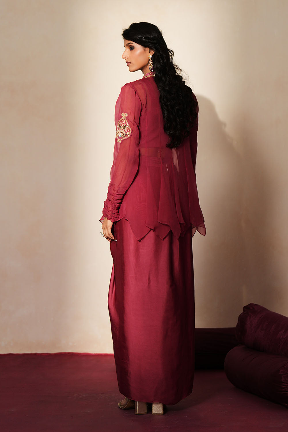 Woman in a mauve pink traditional outfit standing againsta beige wall on a red carpet.