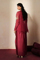 Woman in a mauve pink traditional outfit standing againsta beige wall on a red carpet.