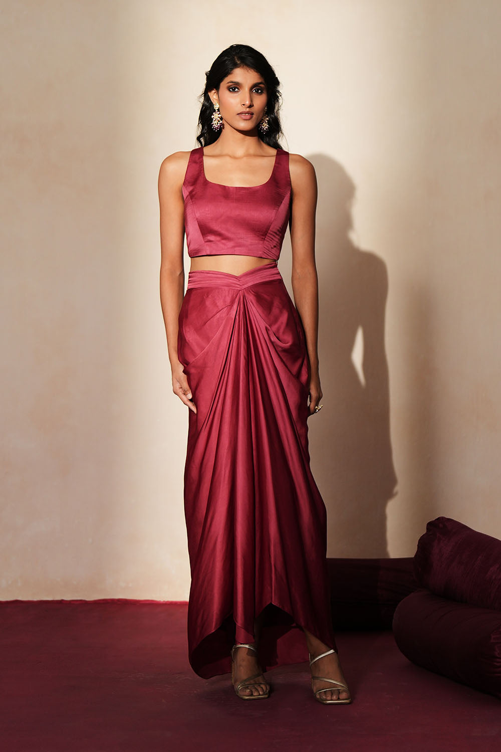 Woman in a mauve pink traditional outfit standing againsta beige wall on a red carpet.