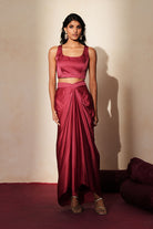 Woman in a mauve pink traditional outfit standing againsta beige wall on a red carpet.