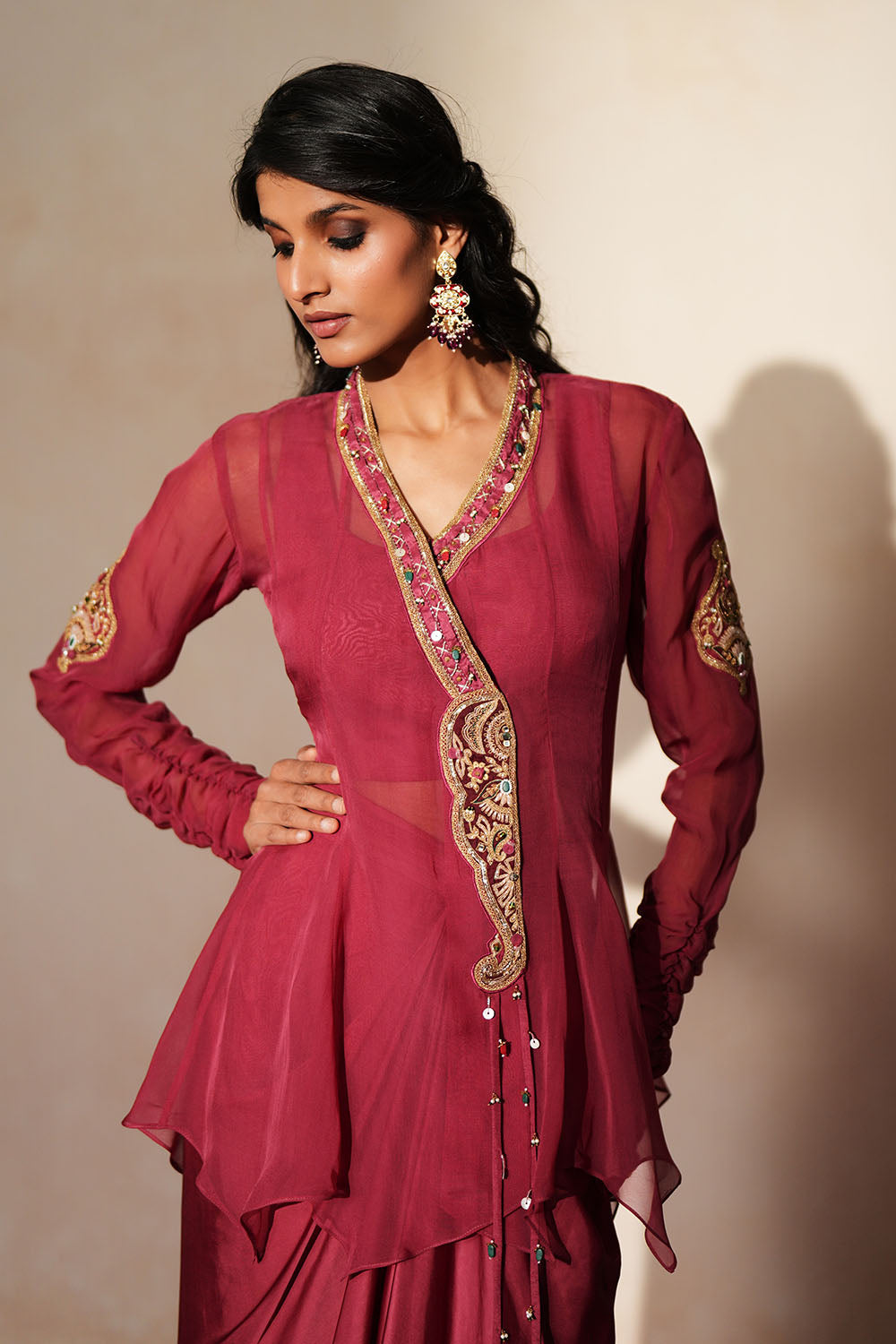 Woman in a mauve pink traditional outfit standing againsta beige wall on a red carpet.