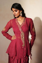 Woman in a mauve pink traditional outfit standing againsta beige wall on a red carpet.