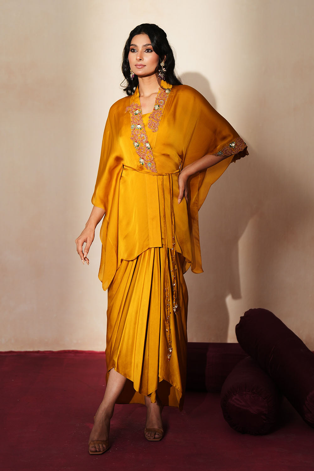 Woman in a golden yellow traditional outfit standing againsta beige wall on a red carpet.
