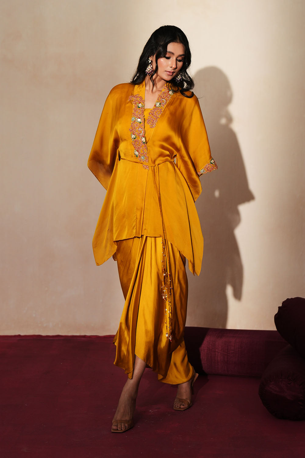 Woman in a golden yellow traditional outfit standing againsta beige wall on a red carpet.