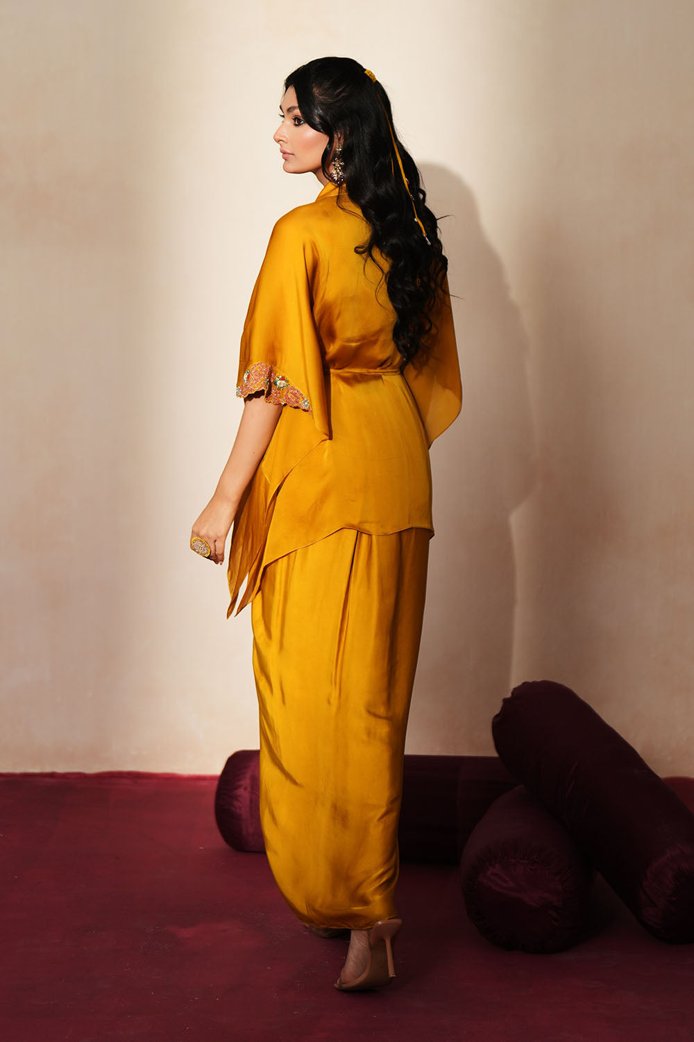 Woman in a golden yellow traditional outfit standing againsta beige wall on a red carpet.