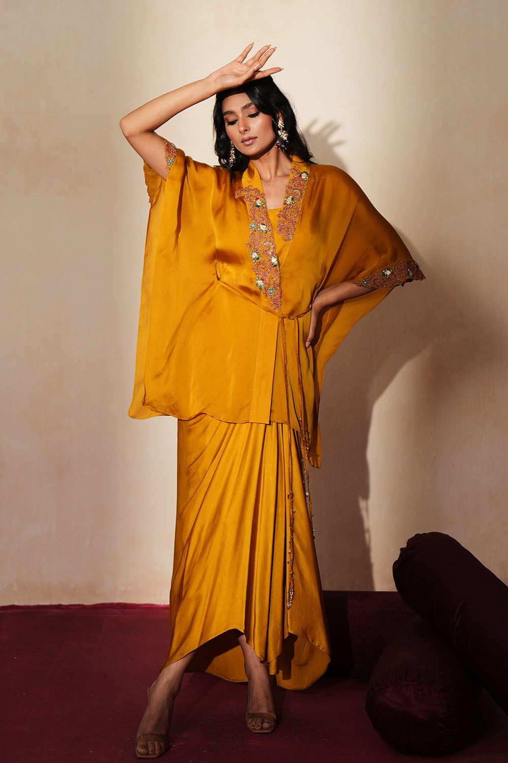 Woman in a golden yellow traditional outfit standing againsta beige wall on a red carpet.