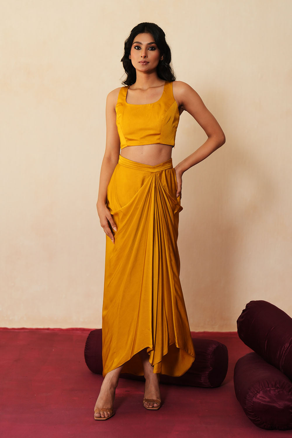 Woman in a golden yellow traditional outfit standing againsta beige wall on a red carpet.
