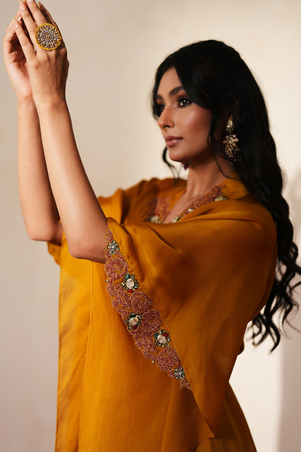 Woman in a golden yellow traditional outfit standing againsta beige wall on a red carpet.
