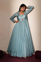 Woman in a pastel blue traditional outfit standing againsta beige wall on a red carpet.