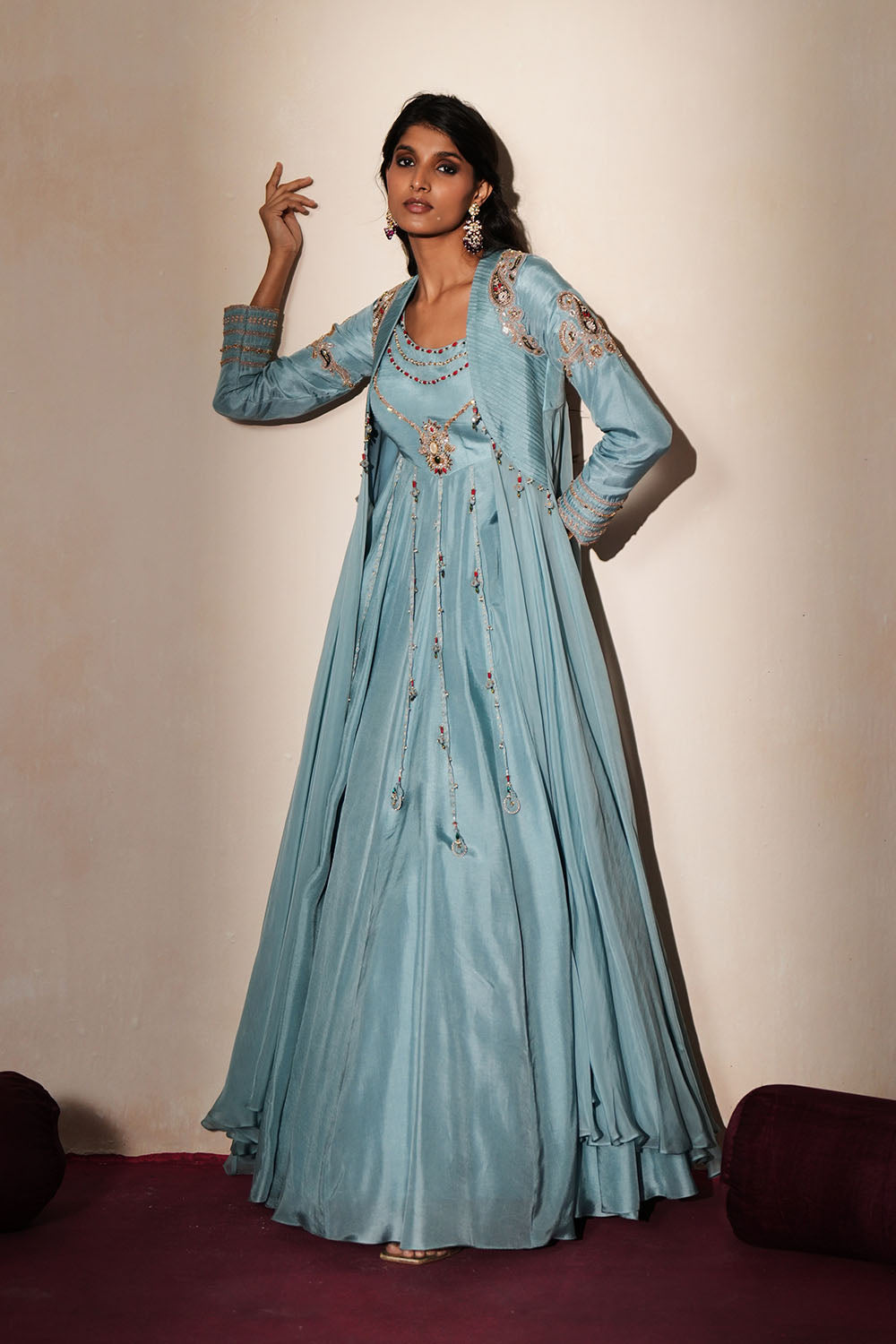 Woman in a pastel blue traditional outfit standing againsta beige wall on a red carpet.