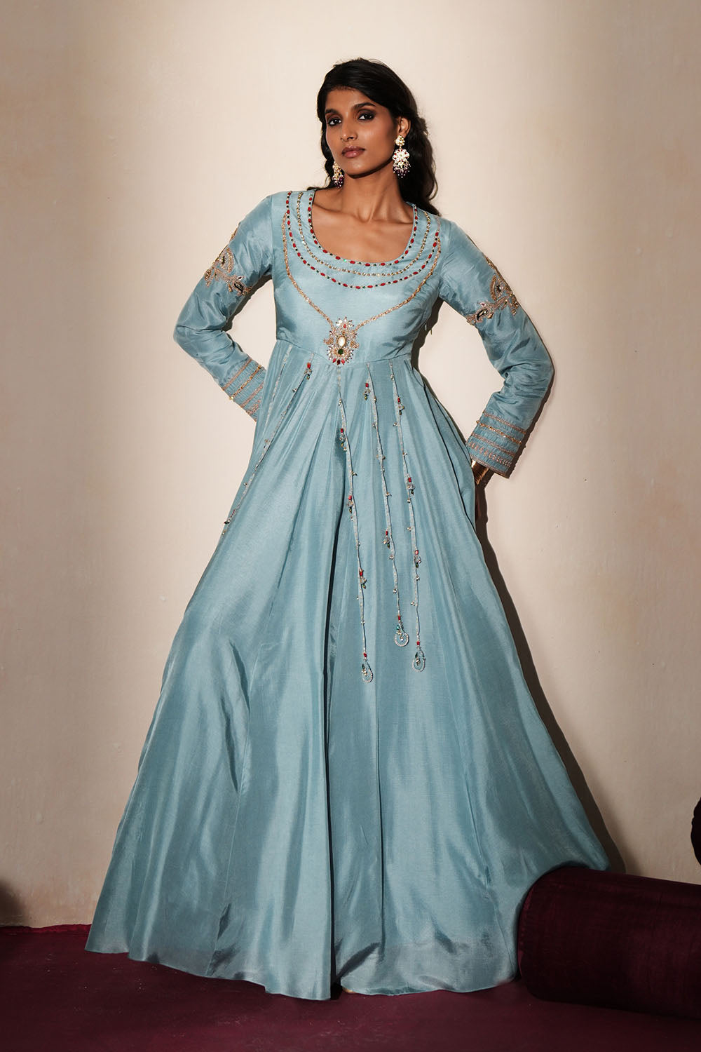Woman in a pastel blue traditional outfit standing againsta beige wall on a red carpet.