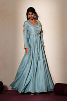 Woman in a pastel blue traditional outfit standing againsta beige wall on a red carpet.