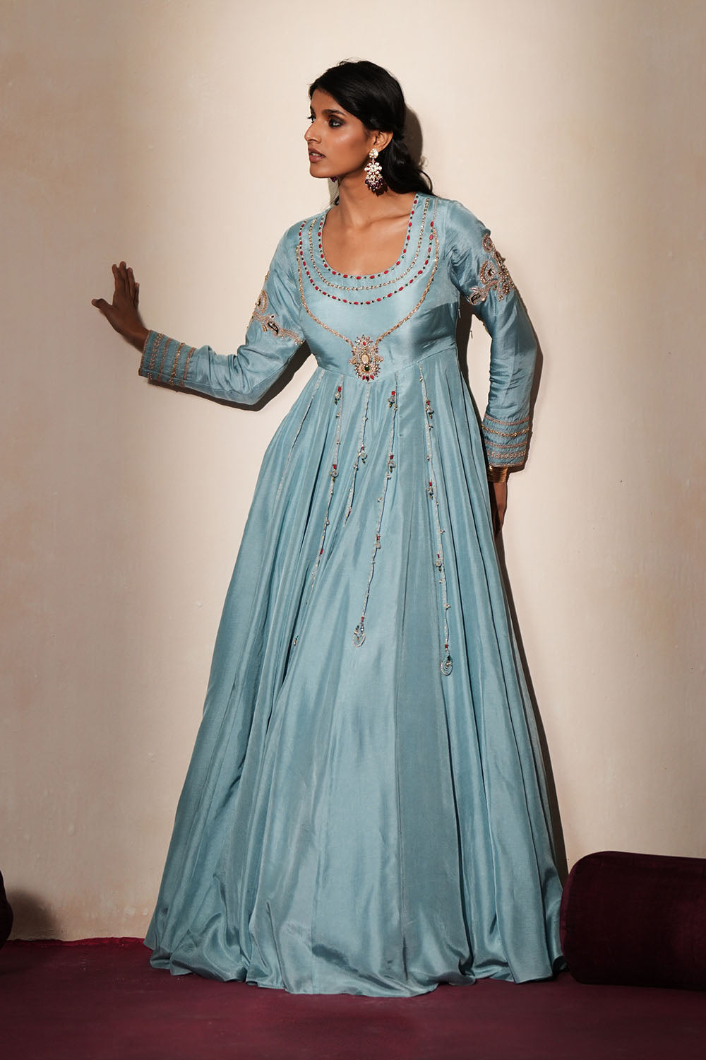 Woman in a pastel blue traditional outfit standing againsta beige wall on a red carpet.