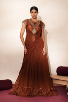 Woman in a mettalic brown traditional outfit standing againsta beige wall on a red carpet.