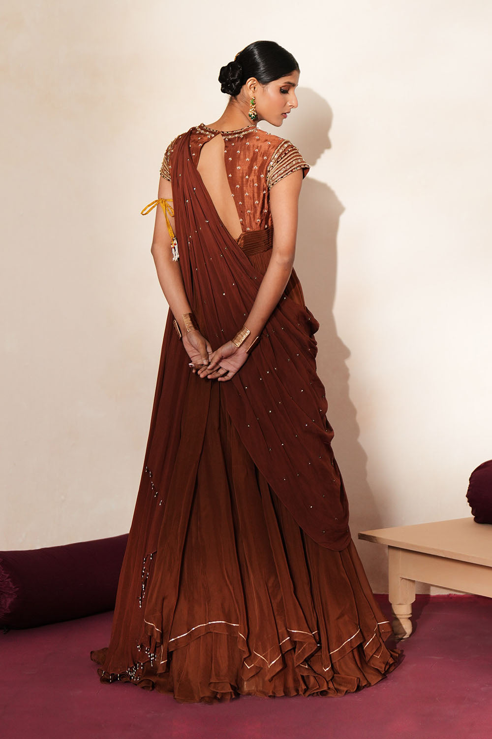 Woman in a mettalic brown traditional outfit standing againsta beige wall on a red carpet.