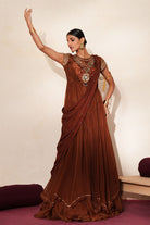 Woman in a mettalic brown traditional outfit standing againsta beige wall on a red carpet.