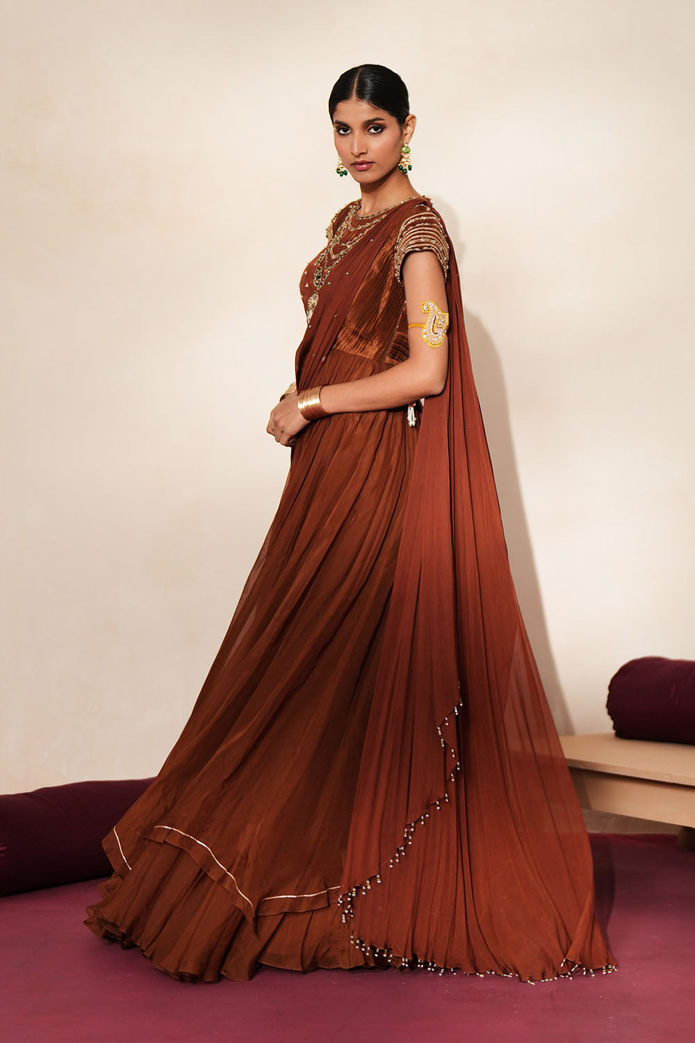 Woman in a mettalic brown traditional outfit standing againsta beige wall on a red carpet.