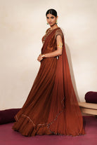 Woman in a mettalic brown traditional outfit standing againsta beige wall on a red carpet.