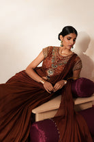 Woman in a mettalic brown traditional outfit standing againsta beige wall on a red carpet.