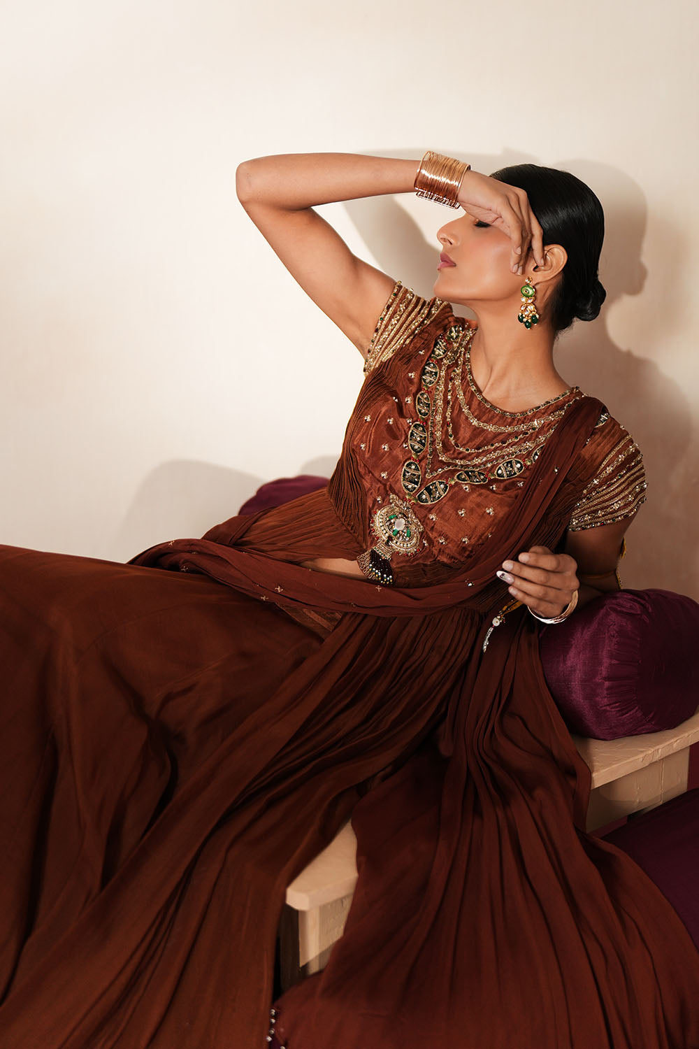 Woman in a mettalic brown traditional outfit standing againsta beige wall on a red carpet.