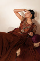 Woman in a mettalic brown traditional outfit standing againsta beige wall on a red carpet.