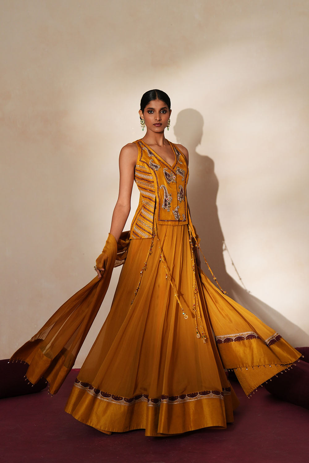 Woman in a golden yellow traditional outfit standing againsta beige wall on a red carpet.