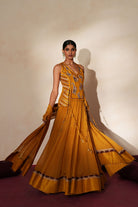 Woman in a golden yellow traditional outfit standing againsta beige wall on a red carpet.