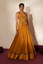 Woman in a golden yellow traditional outfit standing againsta beige wall on a red carpet.