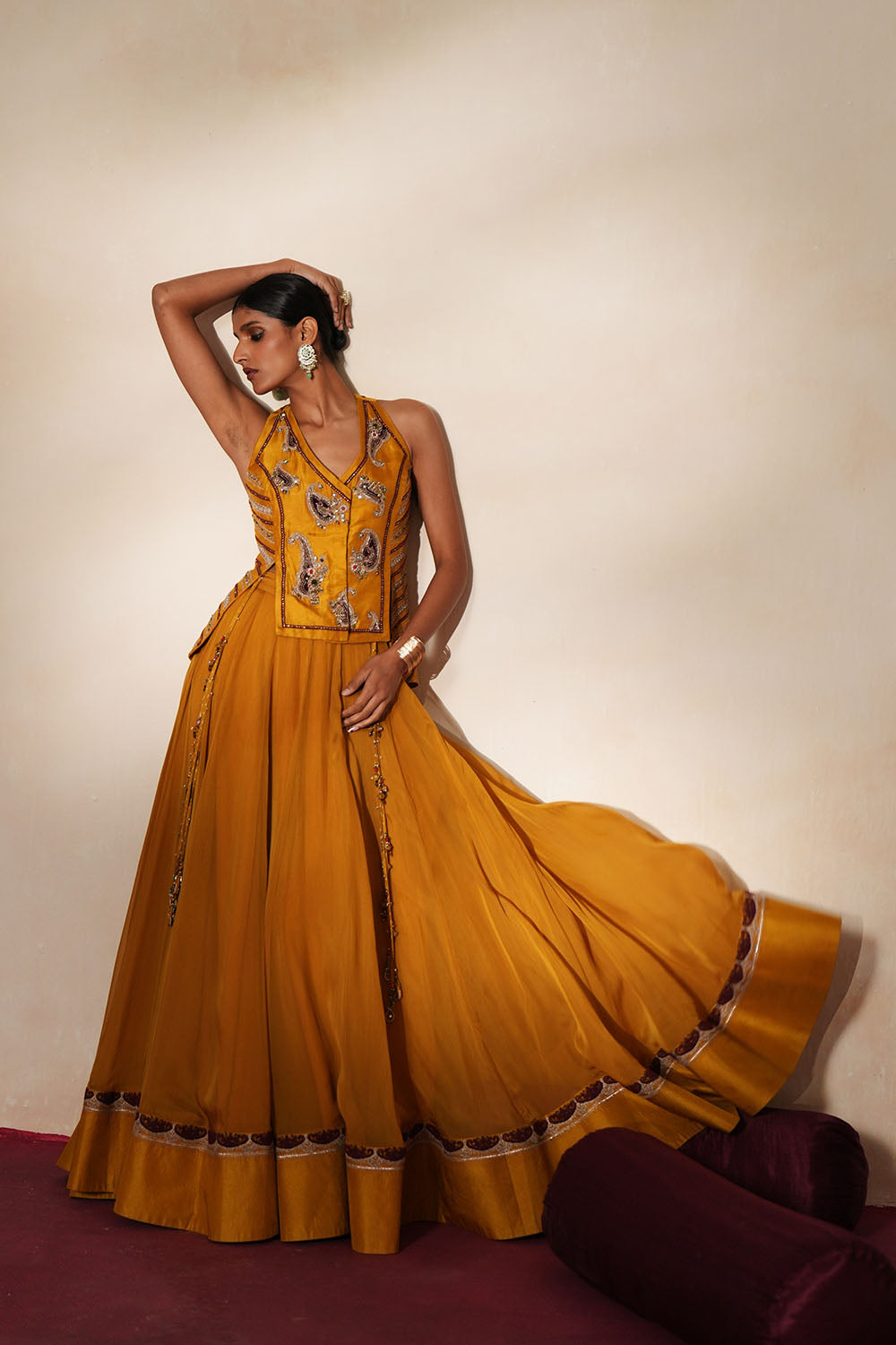 Woman in a golden yellow traditional outfit standing againsta beige wall on a red carpet.