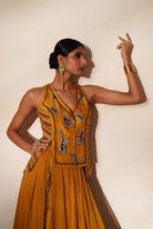 Woman in a golden yellow traditional outfit standing againsta beige wall on a red carpet.