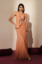 Woman in a metallic mocha  traditional outfit standing againsta beige wall on a red carpet.