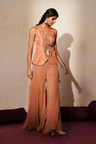 Woman in a metallic mocha  traditional outfit standing againsta beige wall on a red carpet.