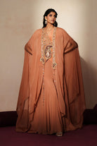Woman in a metallic mocha  traditional outfit standing againsta beige wall on a red carpet.