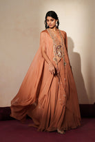 Woman in a metallic mocha  traditional outfit standing againsta beige wall on a red carpet.