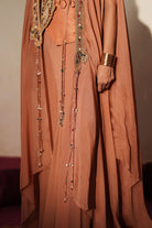 Woman in a metallic mocha  traditional outfit standing againsta beige wall on a red carpet.