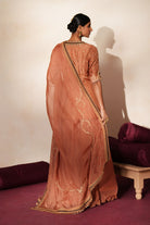 Woman in a metallic mocha  traditional outfit standing againsta beige wall on a red carpet.