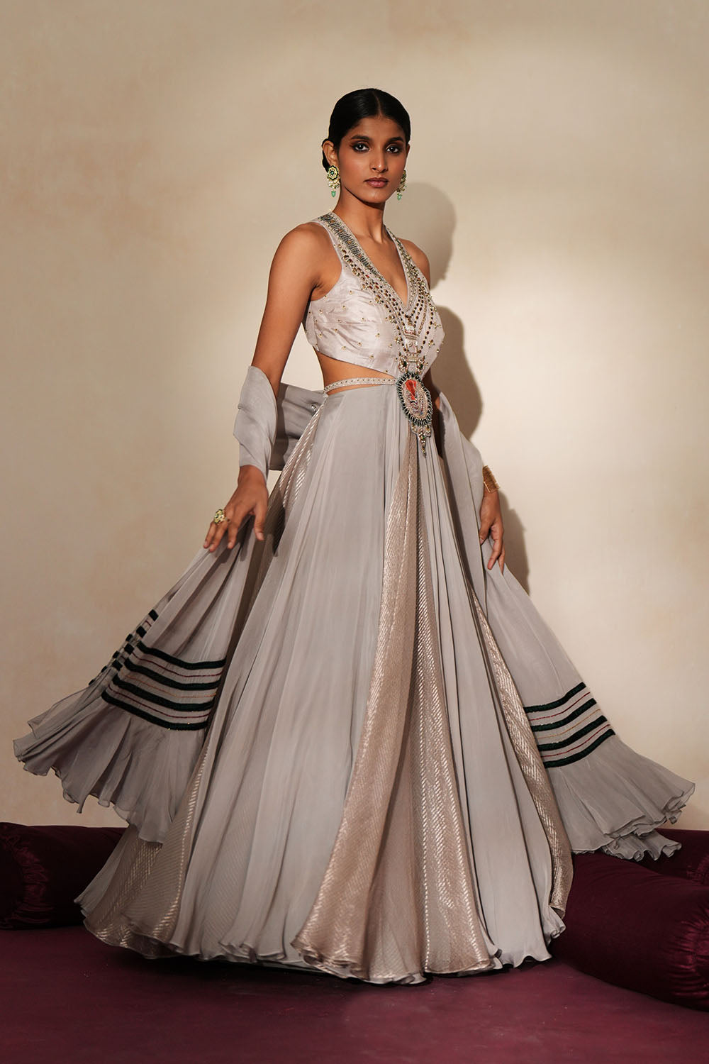 Woman in a mettalic grey traditional outfit standing againsta beige wall on a red carpet.