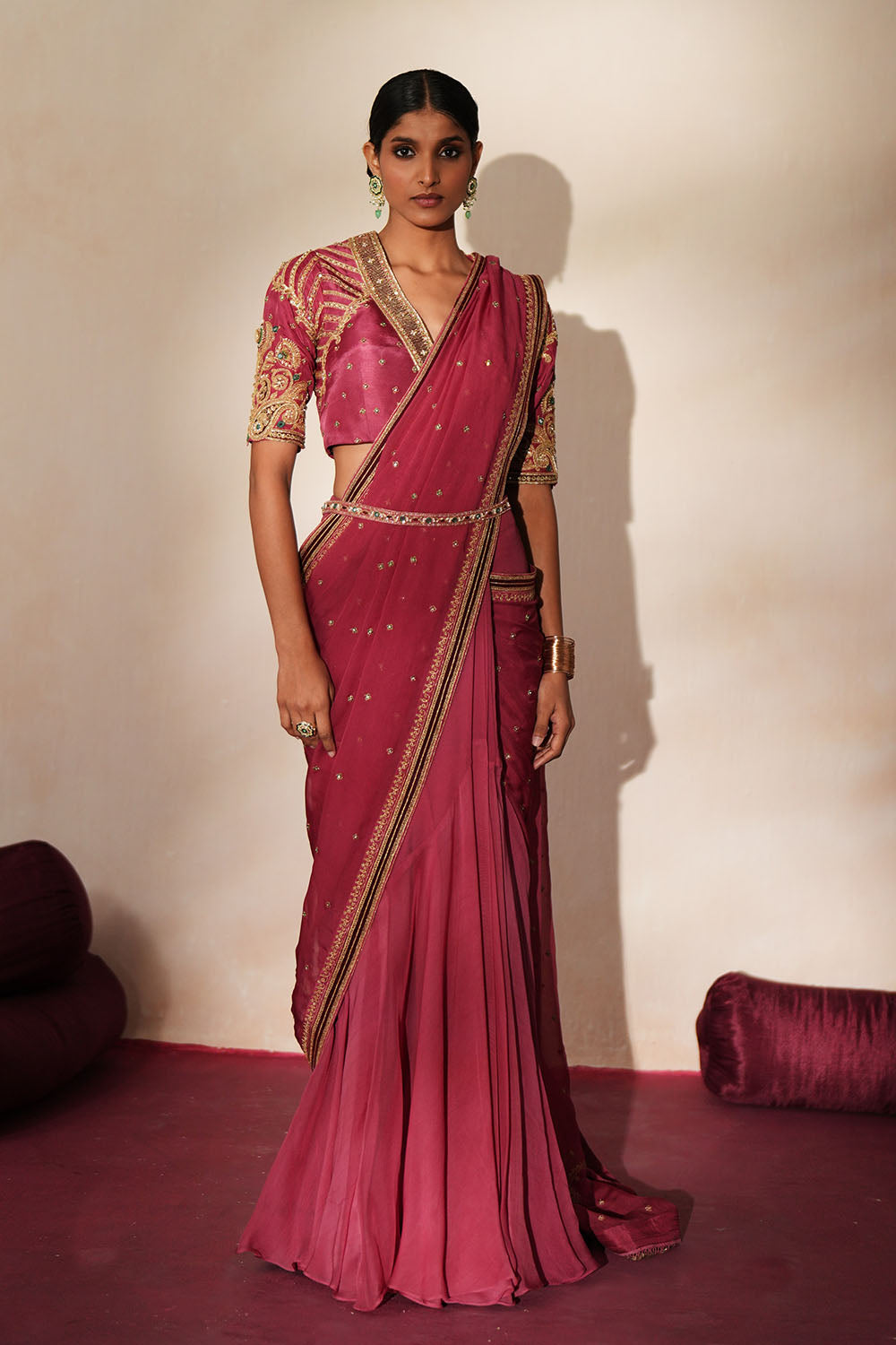 Woman in a mauve pink traditional outfit standing againsta beige wall on a red carpet.