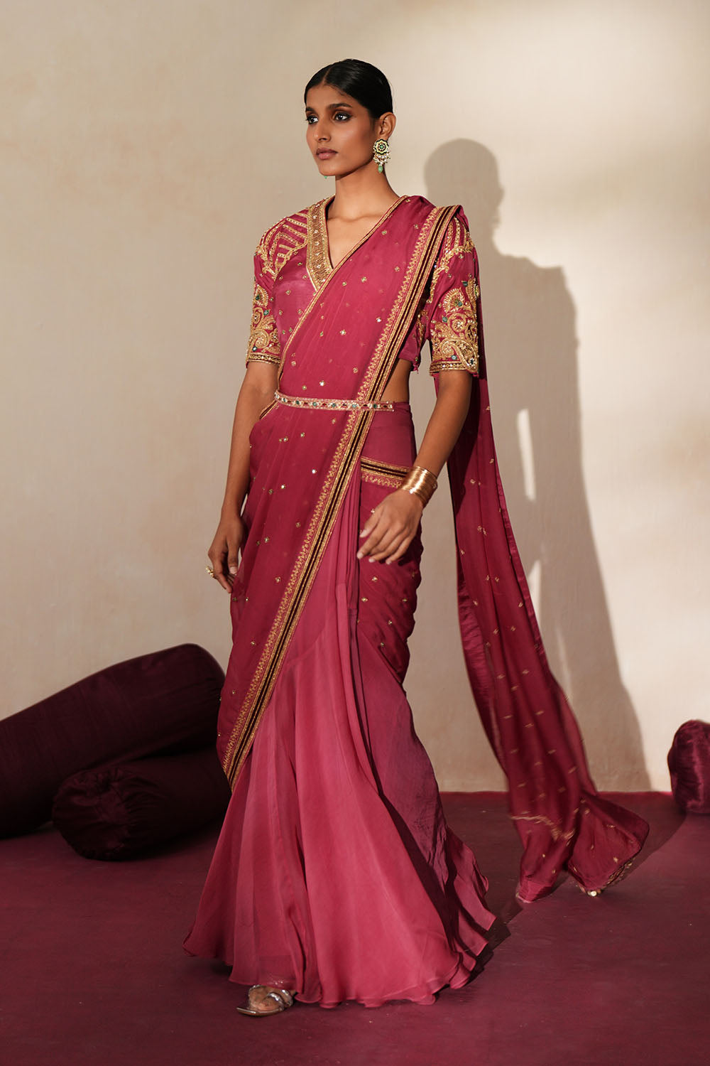 Woman in a mauve pink traditional outfit standing againsta beige wall on a red carpet.