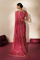 Woman in a mauve pink traditional outfit standing againsta beige wall on a red carpet.