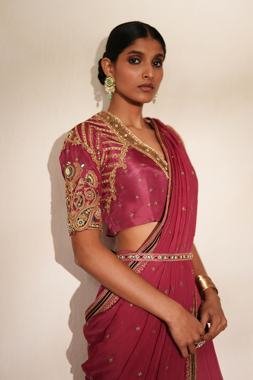 Woman in a mauve pink traditional outfit standing againsta beige wall on a red carpet.