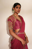 Woman in a mauve pink traditional outfit standing againsta beige wall on a red carpet.