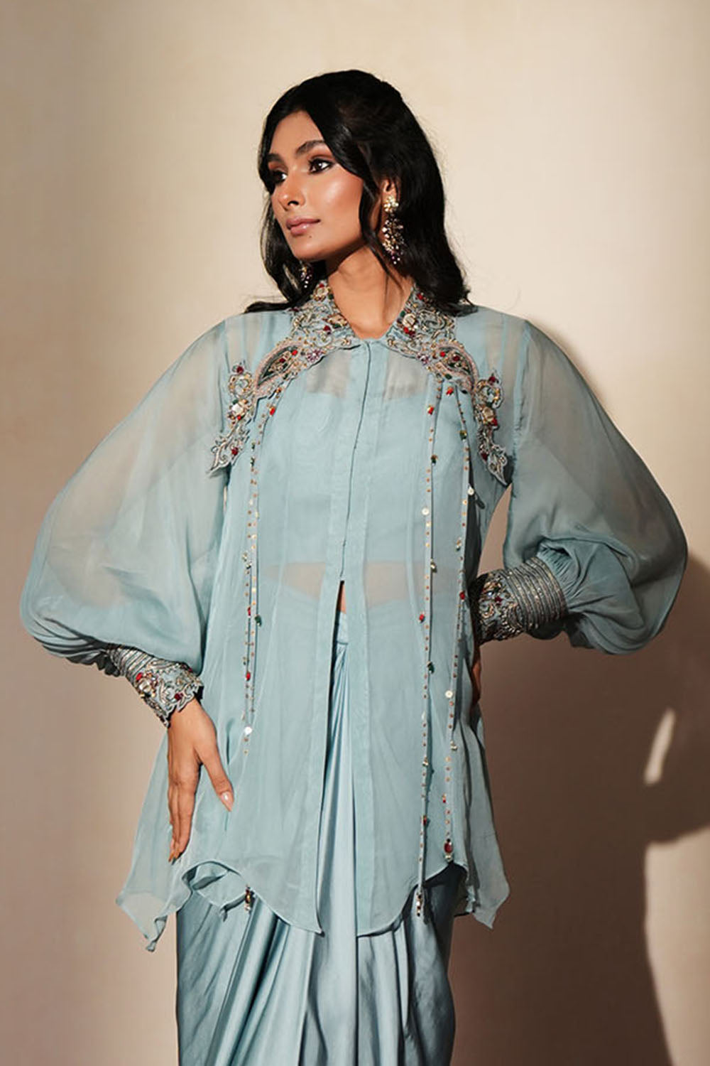 Woman in a pastel blue traditional outfit standing againsta beige wall on a red carpet.