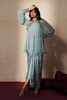 Woman in a pastel blue traditional outfit standing againsta beige wall on a red carpet.