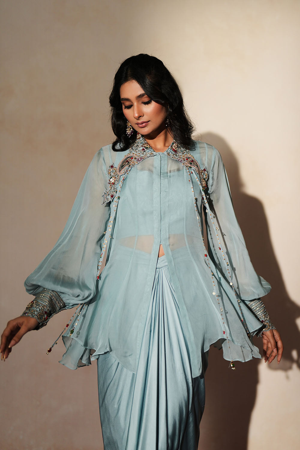 Woman in a pastel blue traditional outfit standing againsta beige wall on a red carpet.