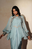 Woman in a pastel blue traditional outfit standing againsta beige wall on a red carpet.