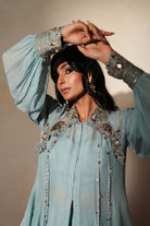 Woman in a pastel blue traditional outfit standing againsta beige wall on a red carpet.