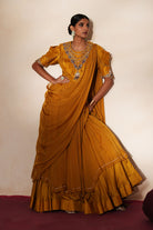 Woman in a golden yellow traditional outfit standing againsta beige wall on a red carpet.