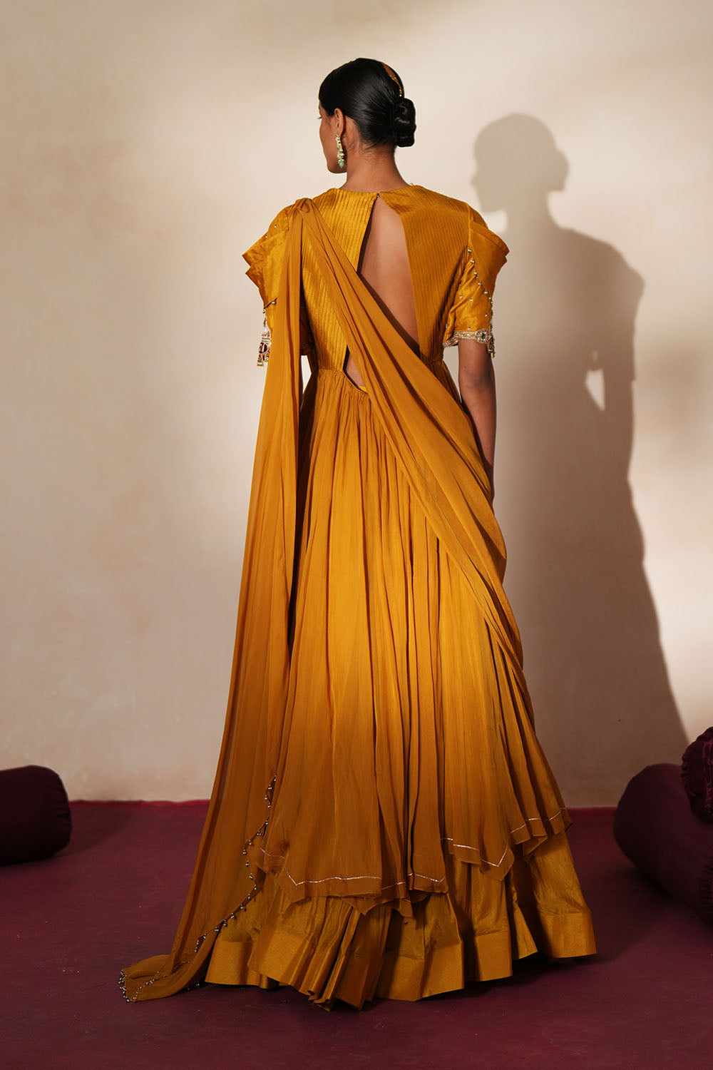 Woman in a golden yellow traditional outfit standing againsta beige wall on a red carpet.